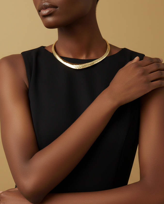 Model wearing a black dress with a gold hammered choker against a beige background